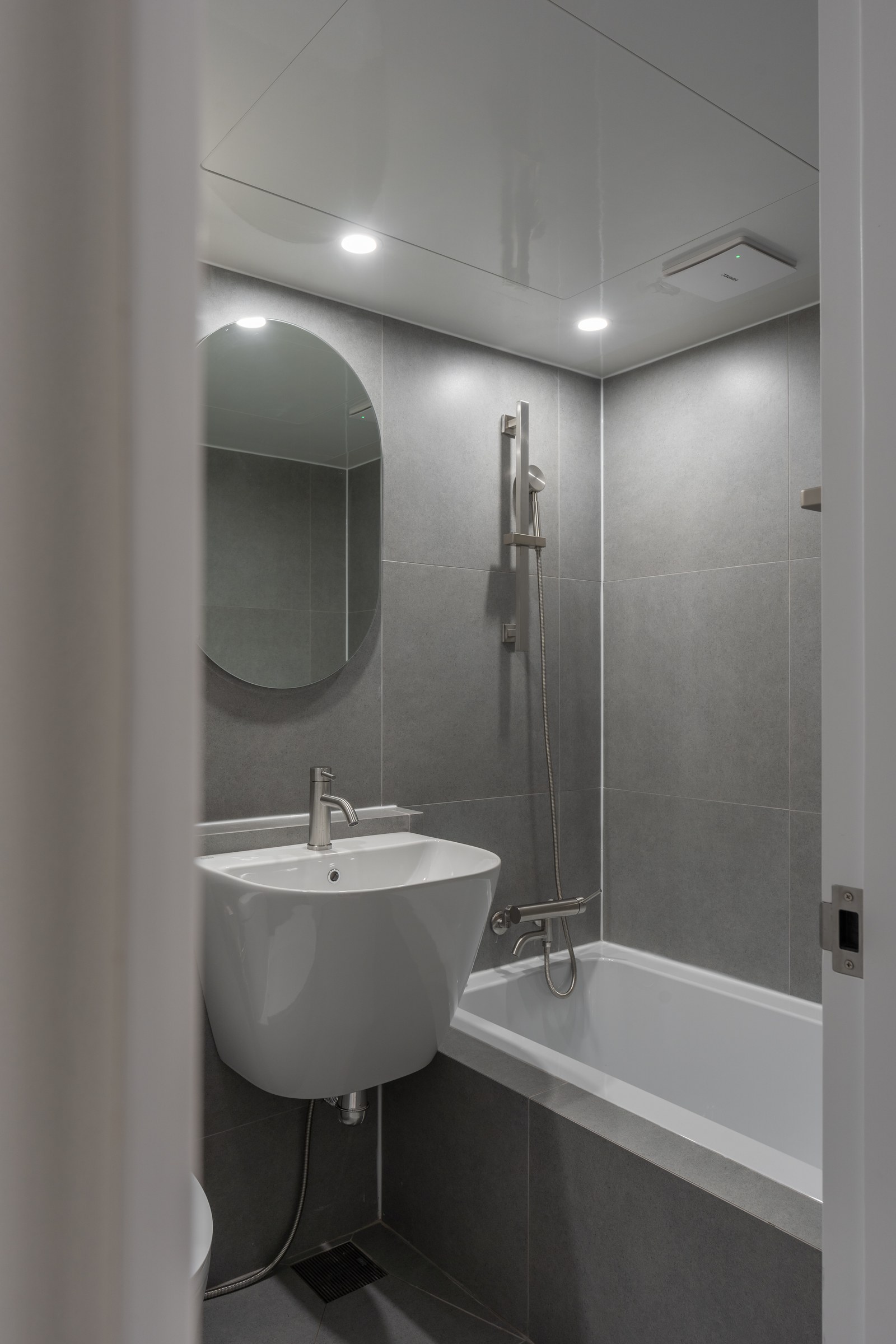 Bathroom composed with grey tile and a curved mirror